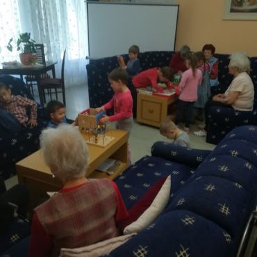 A Liget Otthon nappalija gyermekekkel. A Liget Otthon nappalijában gyermek és szépkorú együtt játszanak.